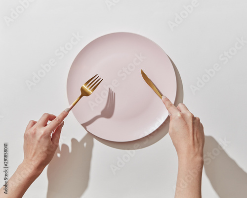 Fork and knife in women's hands with empty plate on a white background, copy space. Waiting for dinner. Flat lay