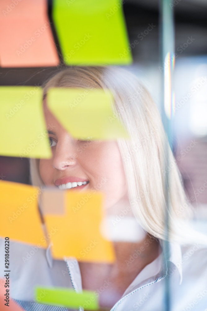 business, startup, planning, management and people concept - happy woman writing on stickers at office glass board business, startup, planning, management and people concept - happy woman writing on stickers at office glass board