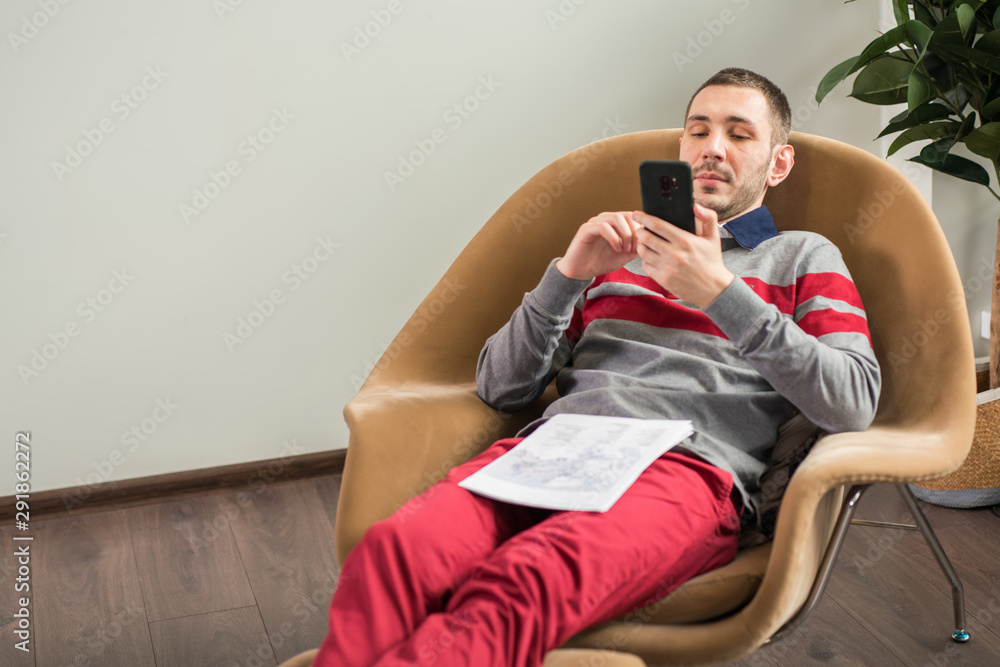 Fototapeta premium Business young man looking his smart phone while, lying on the couch at home or office