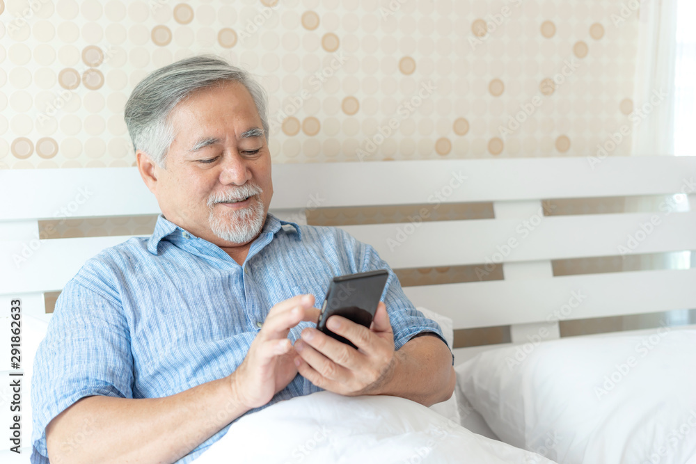 Senior Male using a smartphone , smiling feel happy in bed at home - lifestyle senior concept Senior Male using a smartphone , smiling feel happy in bed at home - lifestyle senior concept