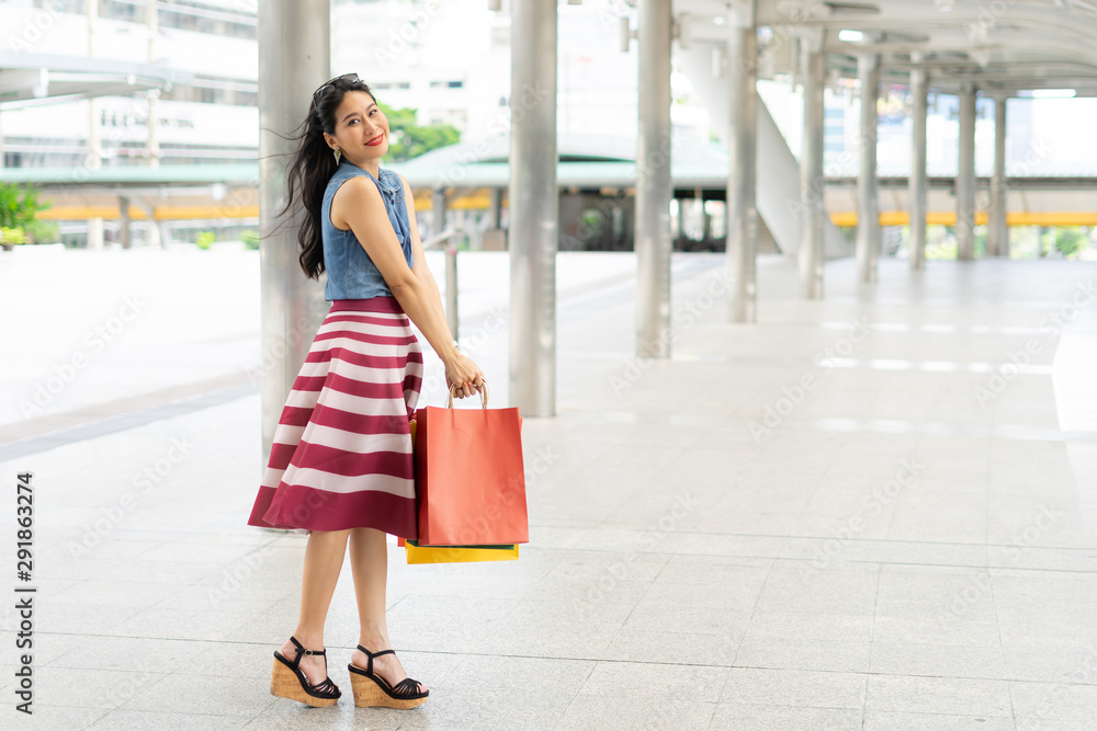 Cheerful young asian woman after shopping and carrying  paper bags