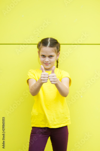 Portrait of a girl in a yellow T-shirt and purple jeans on a background of a yellow wall.
