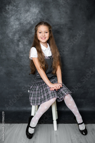 Portrait of a cute little kid girl on a gray background. Child schoolgirl looking at the camera. The concept of education. Copy space.
