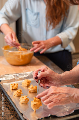 A grandmother and her adult granddaughter scoop and place cookie dough on a cookie sheet. photo