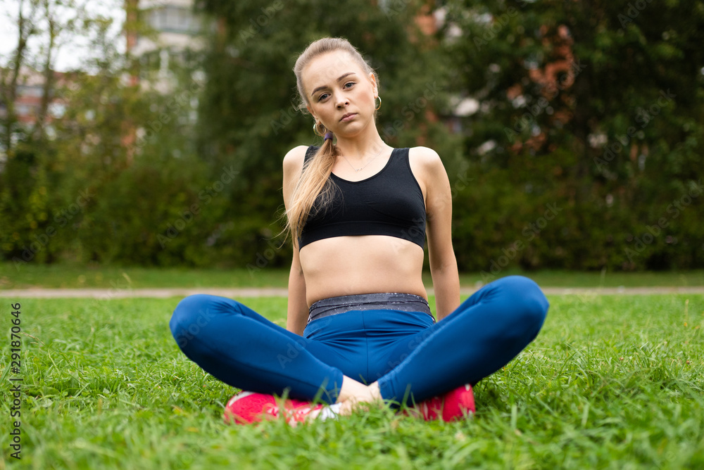 Beautiful athletic girl in a topic sitting on the grass in a relaxed lotus position.