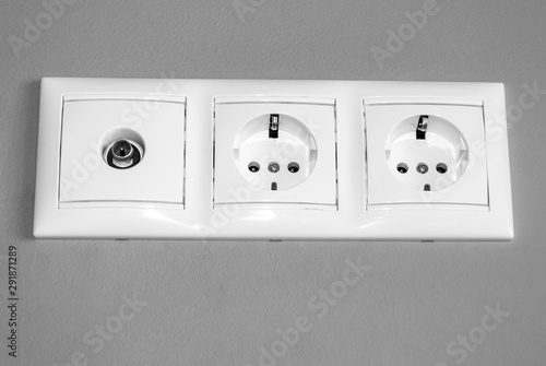 electrical outlets, a set of three white empty electrical sockets for appliances and an antenna connector for a TV on an empty gray