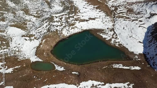 Mountain lake among the snowy peaks. Lake at an altitude of 3377 m. Beautiful panorama of snowy mountains, white clouds, green water of the lake. Flying in the mountains on a drone. Almaty, Kazakhstan photo