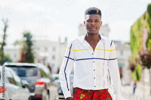 Portrait of handsome stylish african american model man in red throusers and white shirt posed at street. photo