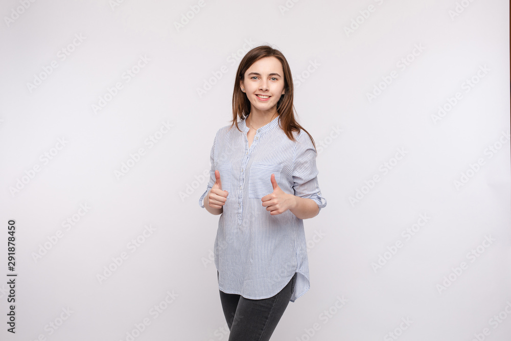 Studio portrait of pretty brunette woman in shirt showing thumbs up and smiling at camera with pleasure and satisfaction. Isolate on white. Studio portrait of pretty brunette woman in shirt showing thumbs up and smiling at camera with pleasure and satisfaction. Isolate on white.