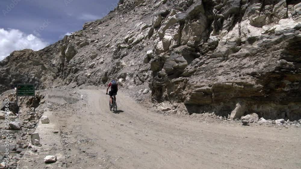 A biker passes through a dirt road at Ladakh in the Himalayan mountains of India. Full shot. A biker passes through a dirt road at Ladakh in the Himalayan mountains of India. Full shot.