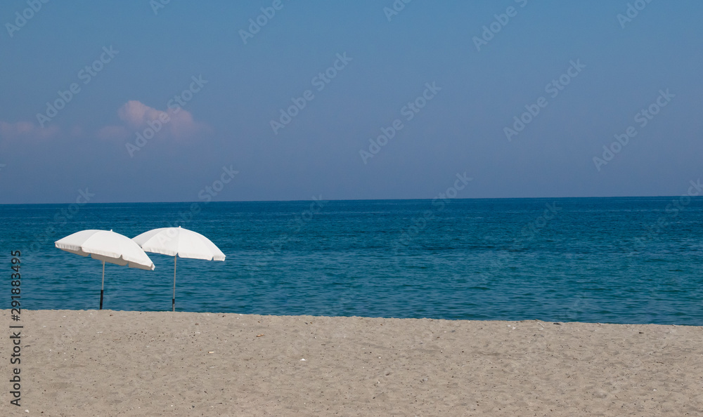 Pair of beach umbrellas on a perfect deserted beach with blue sea and sky in the background