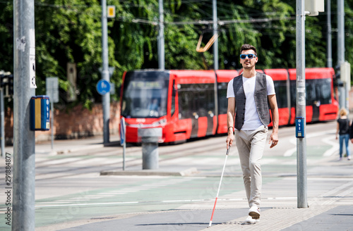 Young blind man with white cane walking across the street in city. photo
