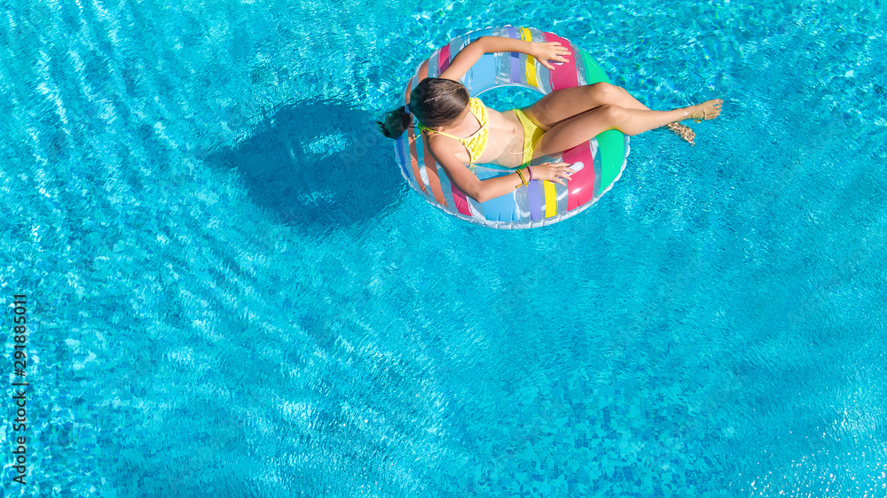 Acrive girl in swimming pool aerial top view from above, kid swims on inflatable ring donut , child has fun in blue water on family vacation resort