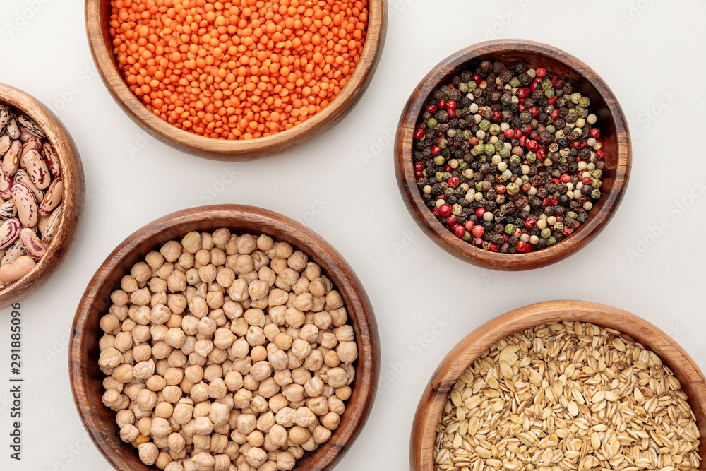 top view of wooden bowls with oatmeal, red lentil, peppercorns and chickpea on white marble surface top view of wooden bowls with oatmeal, red lentil, peppercorns and chickpea on white marble surface