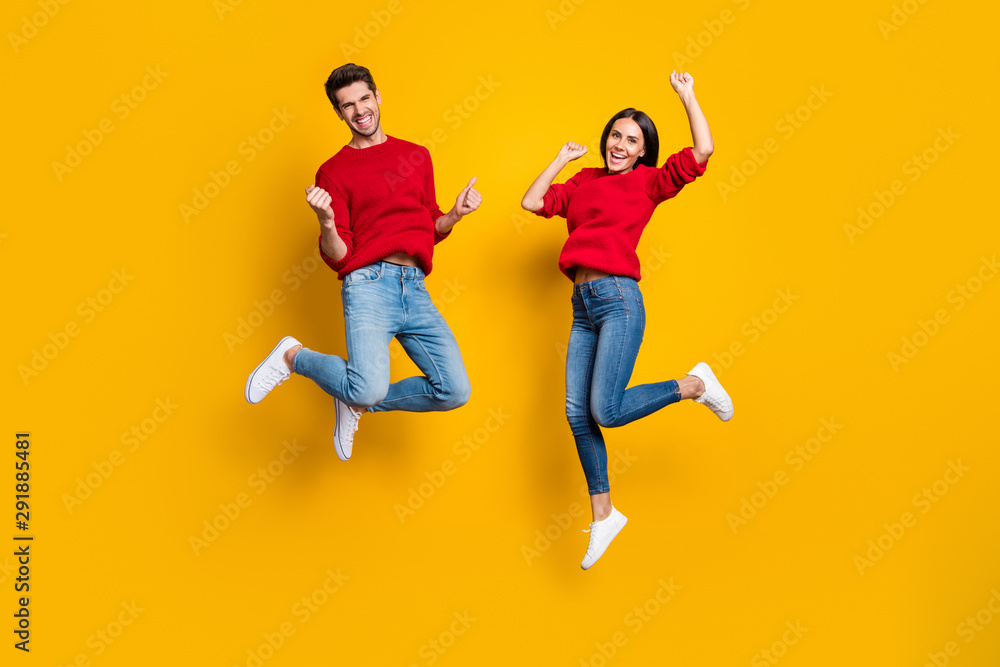 Full length photo of cheerful woman and man jump raise fists scream yes celebrate victory wear red sweater denim jeans isolated over yellow background
