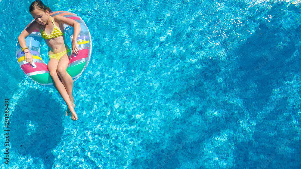 Acrive girl in swimming pool aerial top view from above, kid swims on inflatable ring donut , child has fun in blue water on family vacation resort
