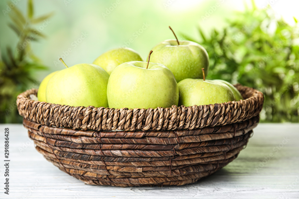Wicker bowl of fresh ripe green apples on white wooden table against blurred background