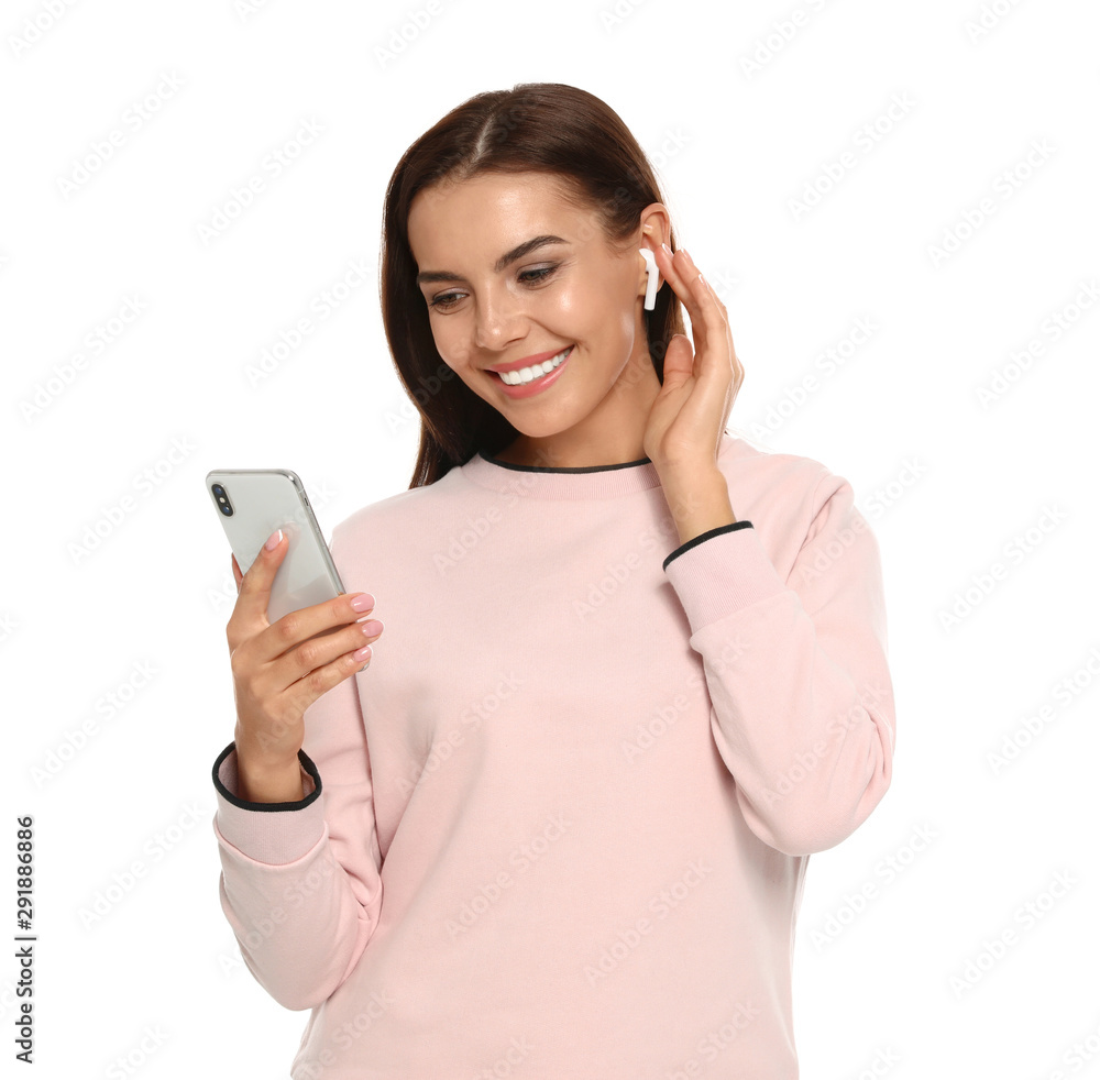 Happy young woman with smartphone listening to music through wireless earphones on white background