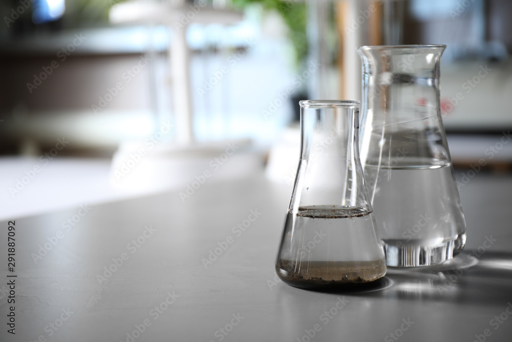Glassware with soil extract and water on grey table, space for text. Laboratory research Glassware with soil extract and water on grey table, space for text. Laboratory research