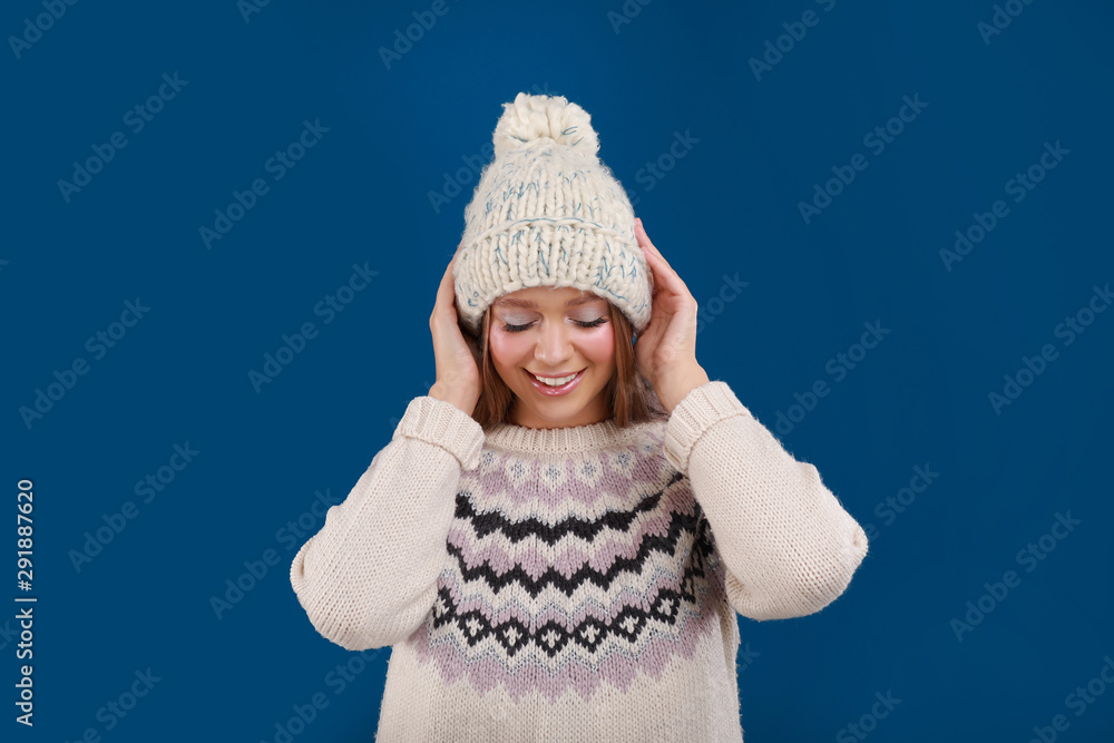 Young woman in warm sweater and hat on blue background. Winter season Young woman in warm sweater and hat on blue background. Winter season