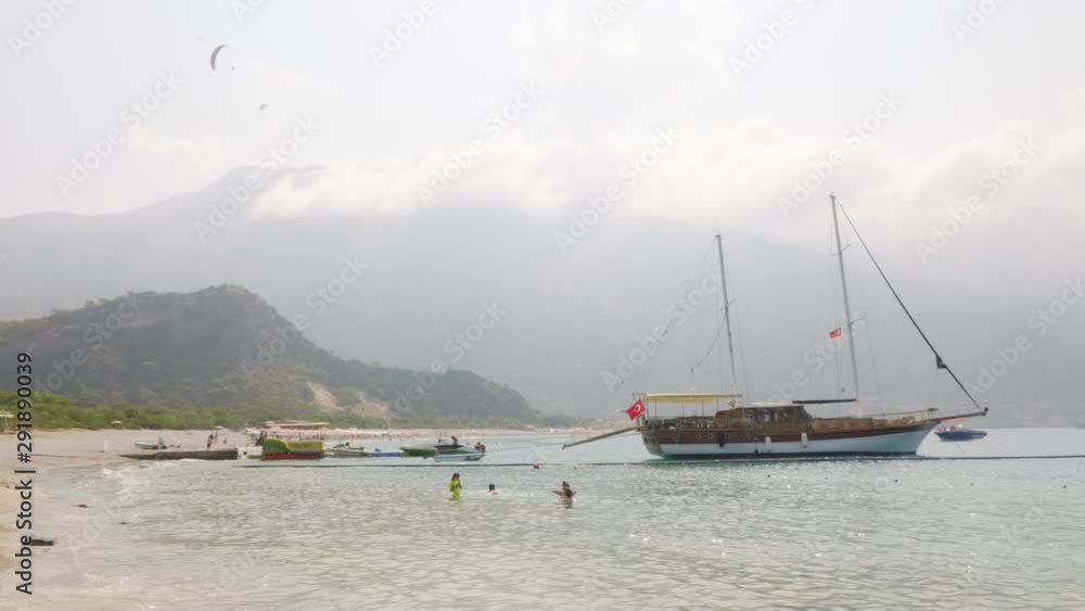 Seashore Beach Boat People Bathe Wood Trees Hills. Sea Coast Scenery Island Bay Ship Foggy Weather Resort Destination. Vacationers Leasure Activity Paraglider Flight Travel Concept 4K