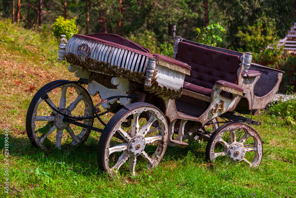 An old carriage made of wood with large wheels without a horse on a mountainside on green grass. Retro and vintage from the story.