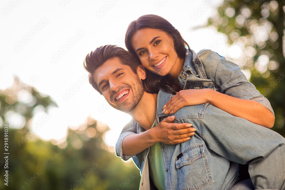 Fototapeta premium Close up photo of pretty girl and guy cuddling piggyback wearing denim jeans outdoors