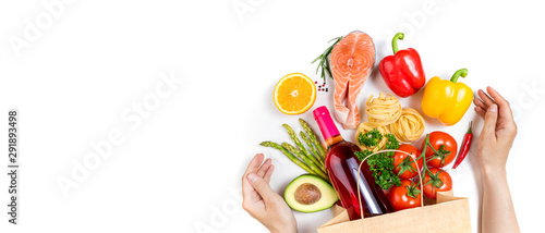 Healthy food in paper bag fish, pasta, vegetables, fruits and wine on white background. Shopping healthy food and female hands. Healthy eating, shopping food supermarket concept. Top view 