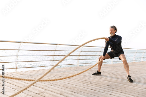 Image of concentrated old man doing exercise with battle ropes