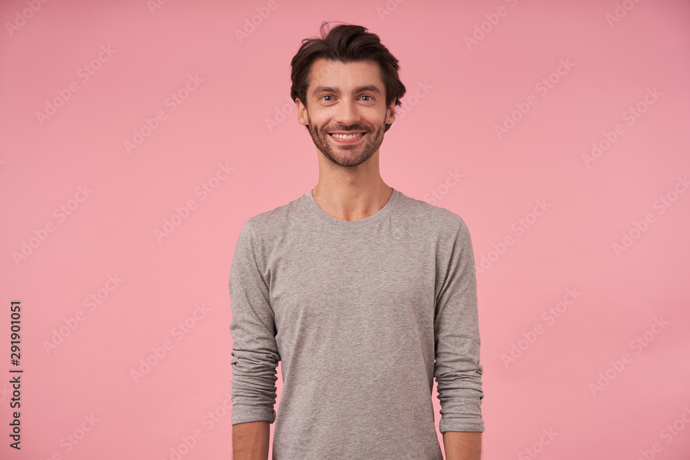 Studio shot of beautiful bearded male with dark hair standing over pink background, wearing casual clothes, looking at camera cheerfully with hands down Studio shot of beautiful bearded male with dark hair standing over pink background, wearing casual clothes, looking at camera cheerfully with hands down