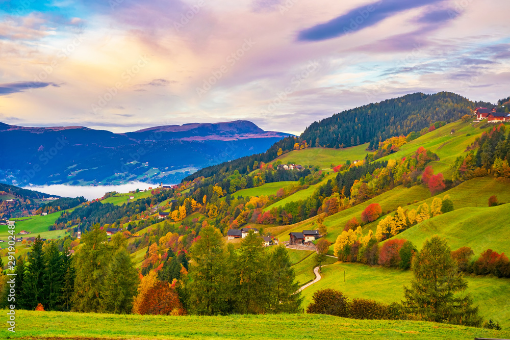 Picturesque autumn scenery with meadows, foliage trees and mountain hills under colorful clouds