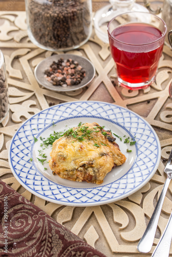 Baked meat with mushroom and mayo cheese sauce and glass of red drink on oriental wooden table Baked meat with mushroom and mayo cheese sauce and glass of red drink on oriental wooden table