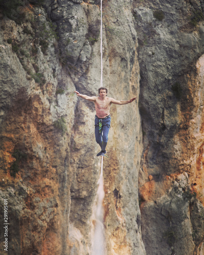 A man is walking along a stretched sling. Highline in the mountains. Man catches balance. Performance of a tightrope walker in nature. Highliner on the background of the mountains.