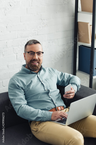 handsome businessman in shirt holding laptop and smartphone in office