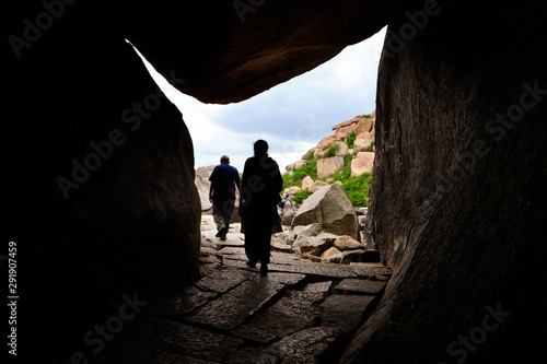 people walking through cave of stone in Hampi