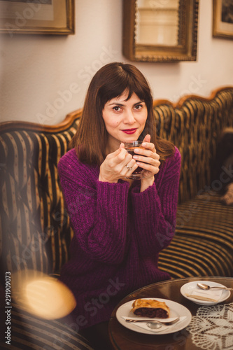 Cozy lifestyle shot of gorgeous European women wearing trendy sweater enjoying aroma and flavor of coffee while relaxing in old cozy cafe