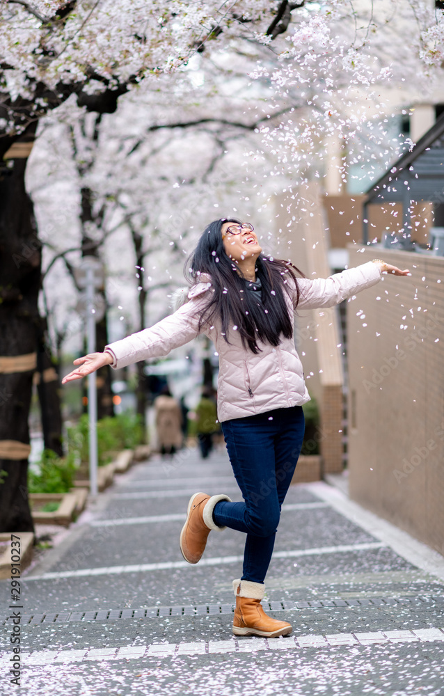 An asian woman enjoy seeing cherry blossom in full bloom in Tokyo, Japan and trowing cherry blossom petals in the air.
