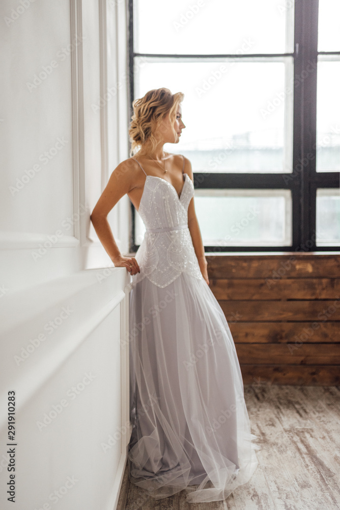 the bride in a beautiful dress stands at the window in the white Studio