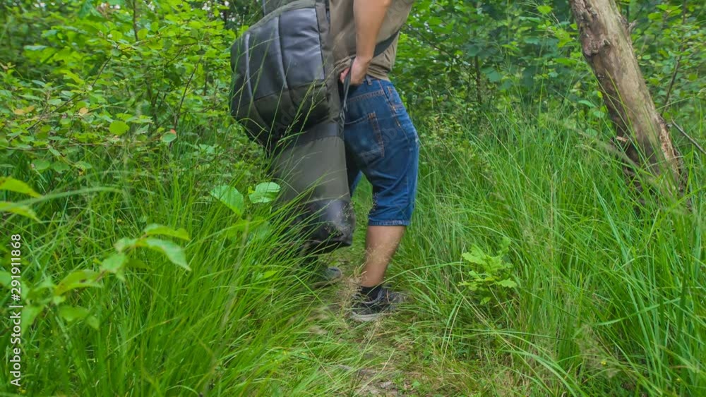 A fisherman is walking in the forest with a fishing equipment. A fisherman is walking in the forest with a fishing equipment.