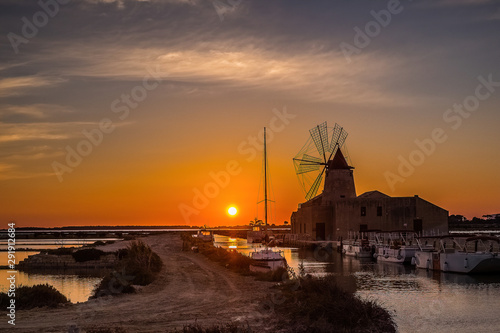 Sunset .Shallow salt pools and windmills Trapani Sicily .The salt from these marshes is considered Italy’s finest and has been big business for centuries; today, only a cottage industry remains