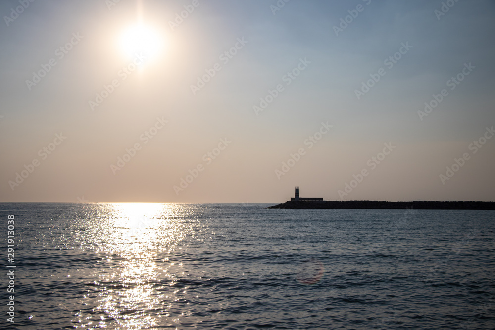 Light house at sunset. Sun rays reflecting on the water of the sea.