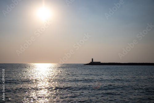 Light house at sunset. Sun rays reflecting on the water of the sea. © Josif