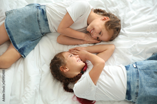 Portrait of cute twin girls lying on bed, top view