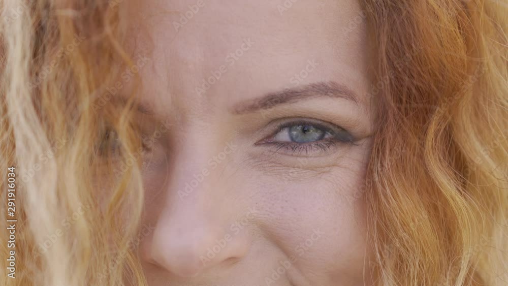 Extreme close-up face of mature red-haired woman with curly hair smiling happily looking at camera. Natural beauty concept. Emotions, happiness, good mood Extreme close-up face of mature red-haired woman with curly hair smiling happily looking at camera. Natural beauty concept. Emotions, happiness, good mood