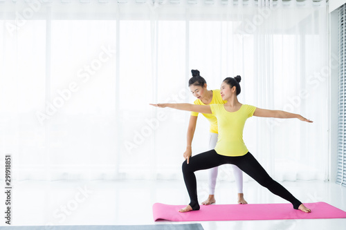 Fototapeta Naklejka Na Ścianę i Meble -  Two young Asian women workout practicing yoga in yellow dress or pose with a trainer and practice meditation wellness lifestyle and health fitness concept in a gym.