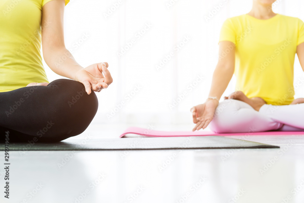 Close-up of Two young Asian women workout practicing yoga in yellow dress or pose with a trainer and practice meditation wellness lifestyle and health fitness concept in a gym.