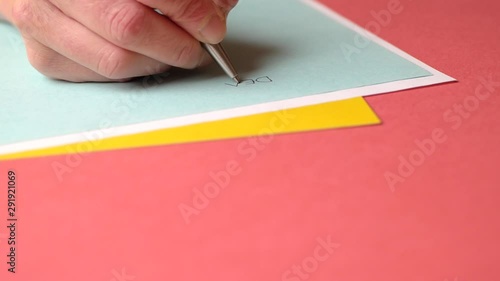 Hand with silver pen writing letter to Santa Claus on colored paper. Close up