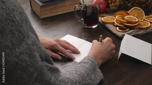 Woman writes Christmas greetings on a greeting card. Close up