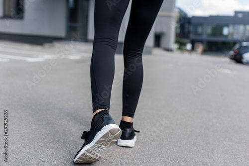 cropped view of sportswoman in black sneakers on street