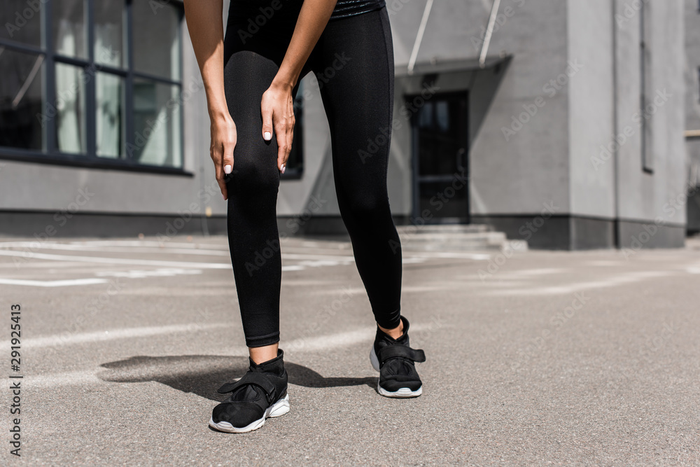 cropped view of sportswoman in black sneakers with knee pain on street cropped view of sportswoman in black sneakers with knee pain on street
